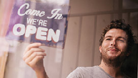 Young man turning over the open sign of his small business.