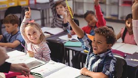 Young children in class smiling and raising their hands.